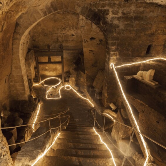 A dimly lit stone staircase with a circular opening at the top, surrounded by stone walls and a rope barrier. 3