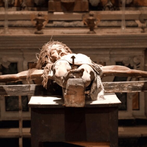 A sculpture of a figure lying on a cross, with a stone structure behind it. 5