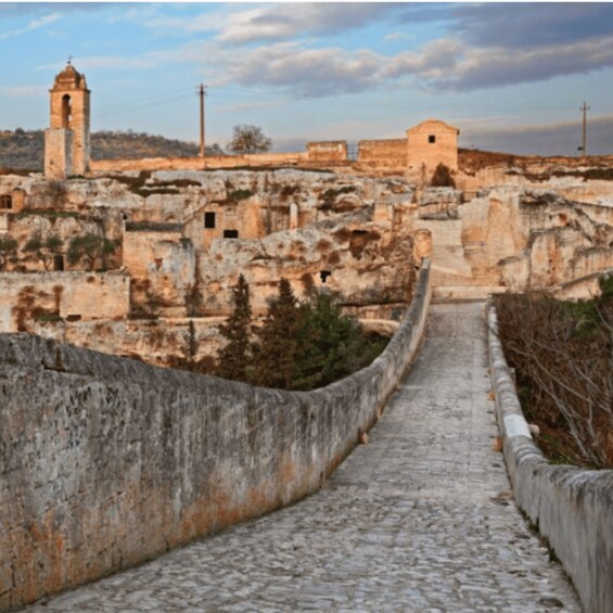 A stone pathway leading through a historic town with old buildings and a bell tower. 2