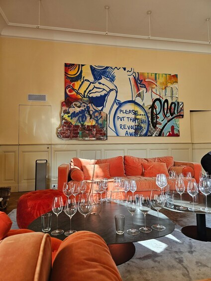 A modern living room with a vibrant abstract painting, a red sofa, and a table set with wine glasses. 1