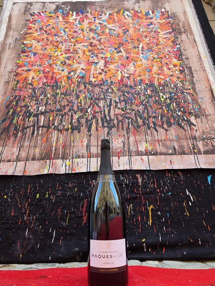 A bottle of champagne in front of a colorful abstract painting. 3
