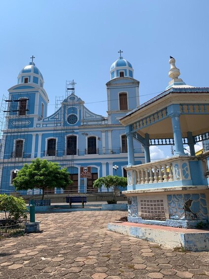 A blue church with two domes and a bell tower, surrounded by a hexagonal paved area and a gazebo. 1