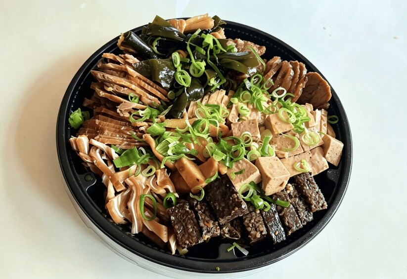 A bowl of assorted food including noodles, tofu, and seaweed, garnished with green onions. 3