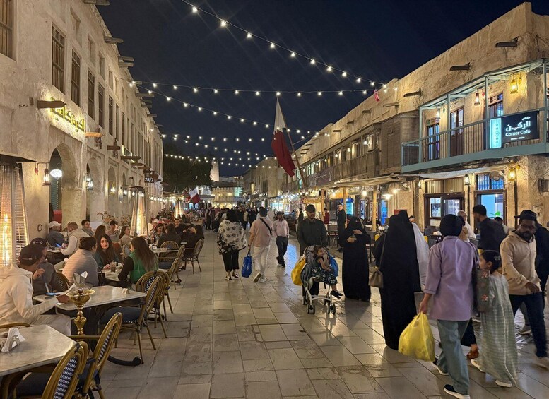 A bustling street at night with string lights, outdoor cafes, and people walking. 2
