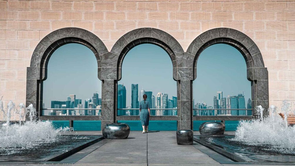 A woman standing in front of three large arched windows overlooking a city skyline. 4