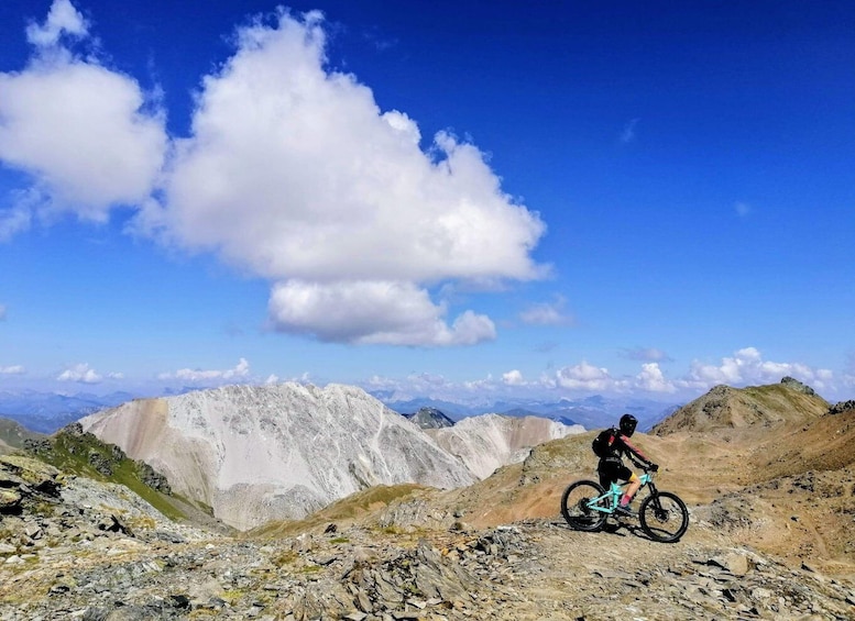 A mountain biker on a rocky trail with a clear blue sky and distant mountains. 2
