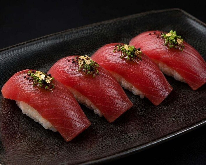 Four pieces of nigiri sushi with salmon on top of rice, garnished with green seaweed and sesame seeds, on a dark plate. 5
