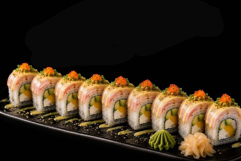 A row of sushi rolls with orange roe and green garnish, arranged on a black plate. 3