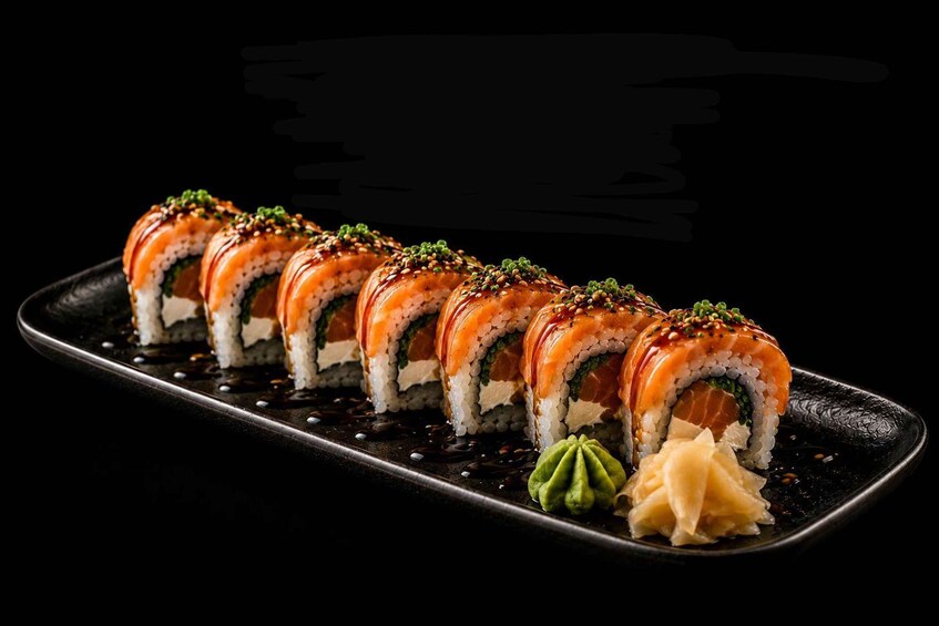 Sushi rolls with salmon and green toppings on a black plate. 2