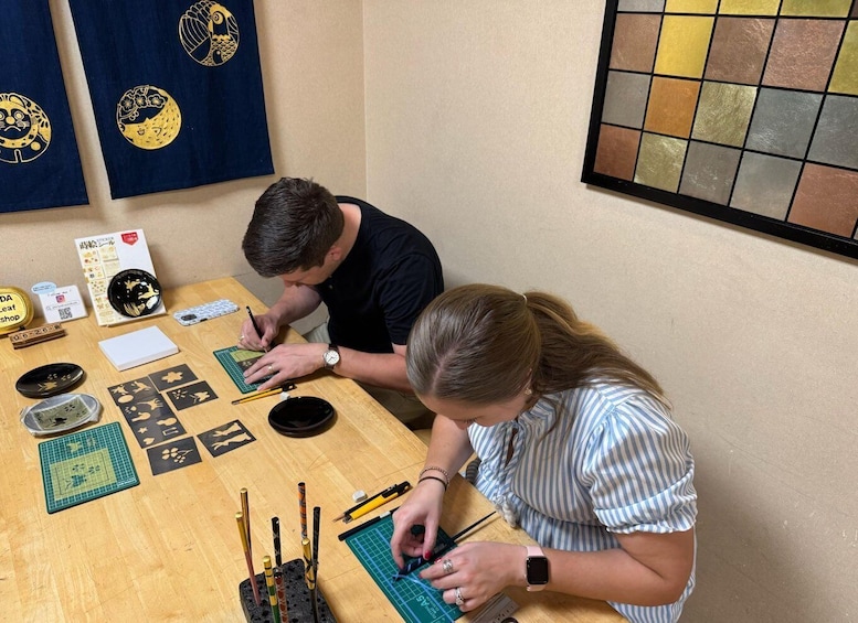 Two people working on a craft project with various tools and materials on a wooden table. 1