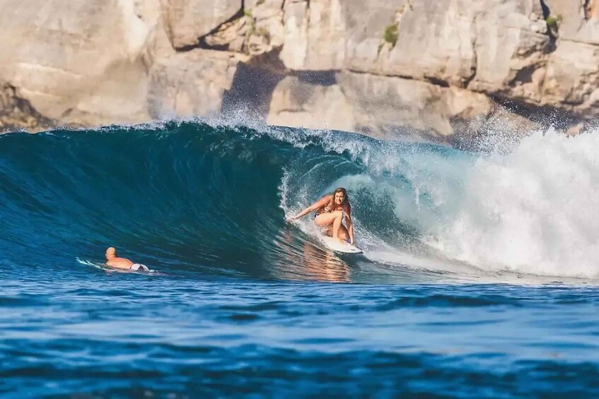 A person surfing a large wave with a rocky cliff in the background. 3