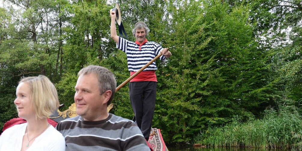 A person in a striped shirt holding a stick, standing on a patterned mat in a wooded area. 2