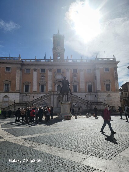 A historic building with a statue in front, people walking around, and a clear sky. 2