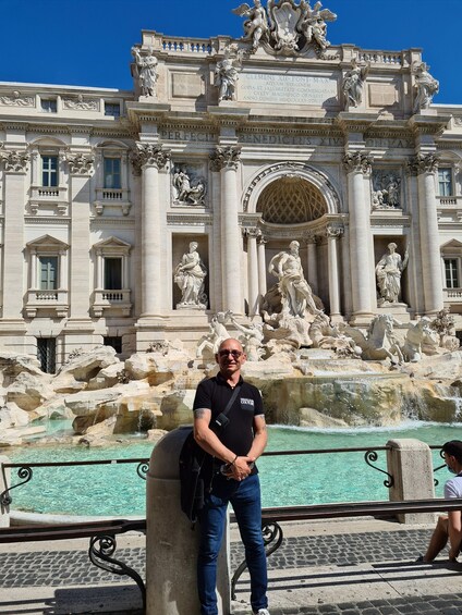 A man standing in front of the Trevi Fountain with the Pantheon in the background. 4