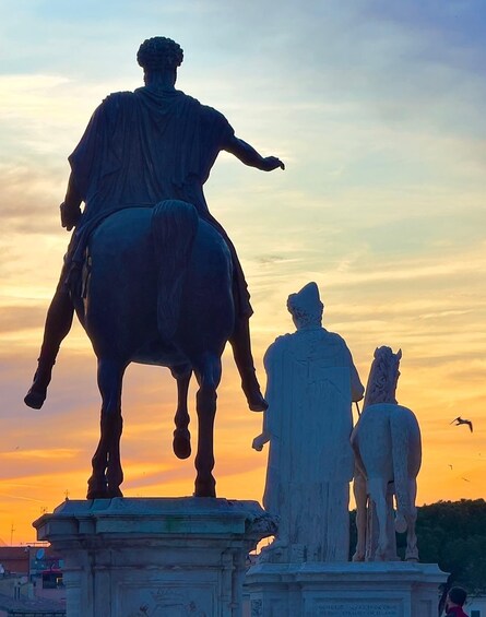 A statue of a figure on horseback with two smaller statues beside it, set against a sunset sky. 5