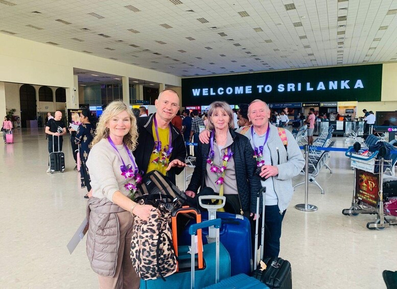 A group of people at an airport with luggage, a sign reading 'WELCOME TO SRI LANKA,' and a terminal with seating areas. 2