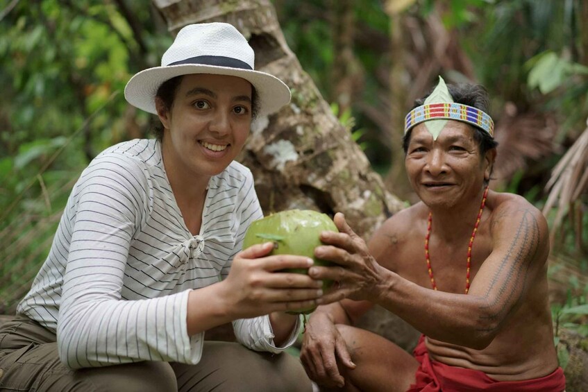 Two people in a forest, one holding a green coconut. 1