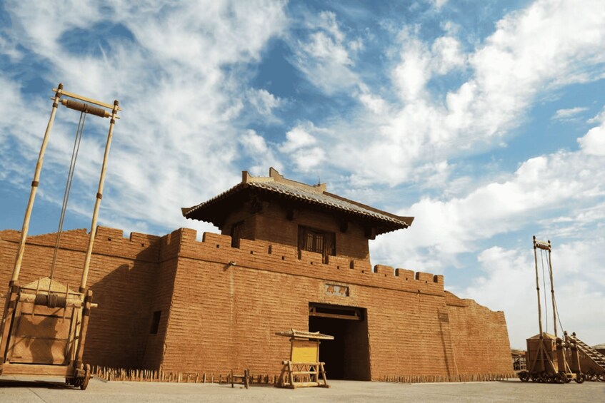 A large brick fortress with a traditional tiled roof, a wooden gate, and a clear blue sky with clouds. 3
