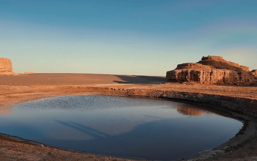 A desert landscape with a large body of water reflecting the sky and a prominent rock formation. 1