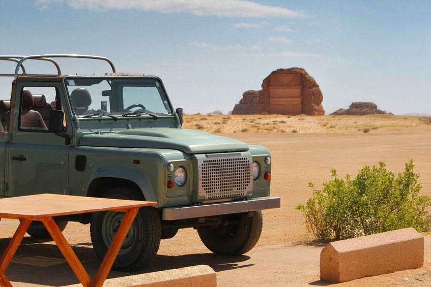 A green off-road vehicle parked in a desert with a wooden table and a small plant nearby. 4