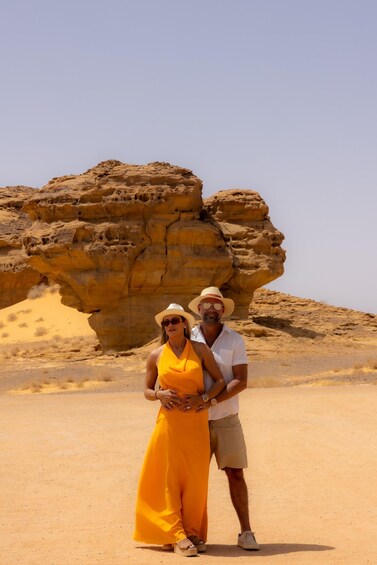 A man and woman in a desert with a large rock formation in the background. 3
