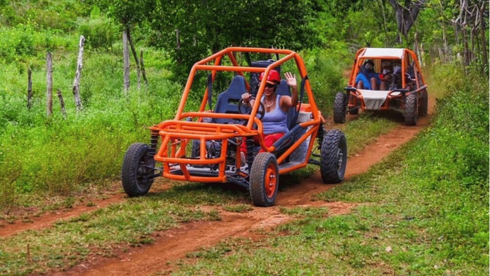 Two orange off-road vehicles on a dirt path surrounded by greenery. 5