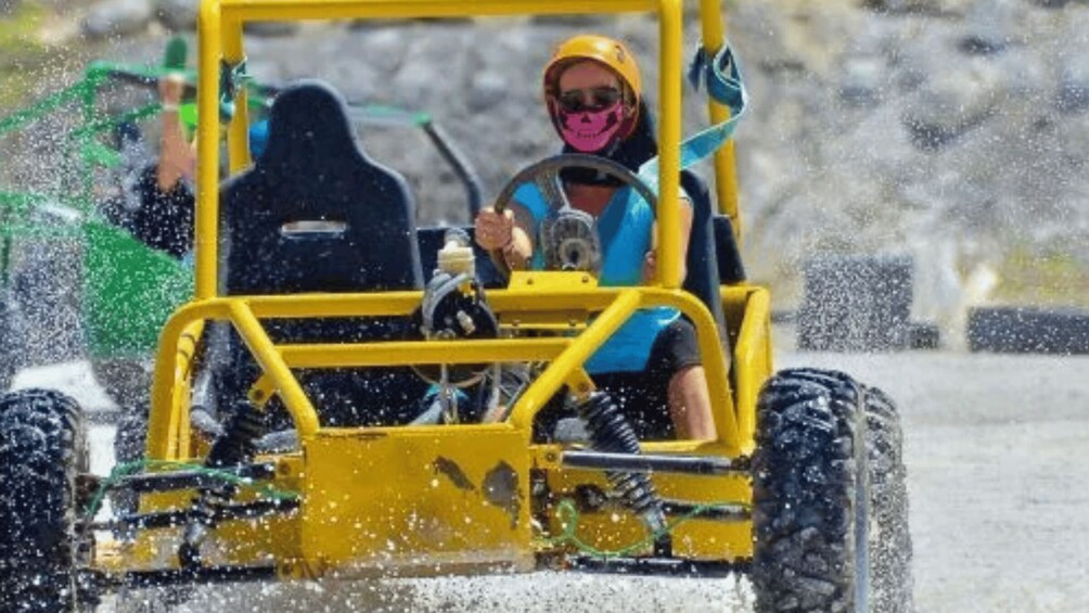 A yellow go-kart with a driver wearing a helmet and sunglasses. 2