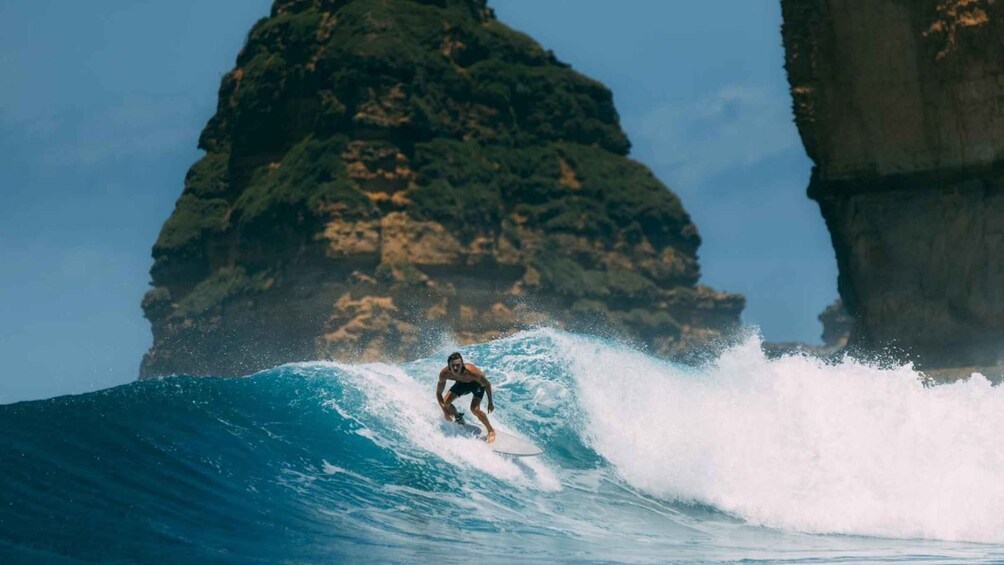 A surfer riding a large wave with a rocky cliff in the background. 1