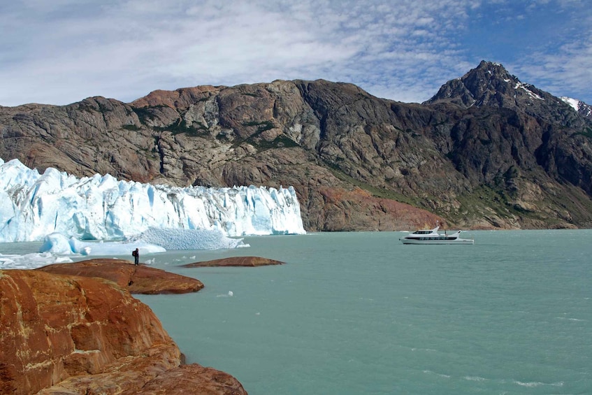 A glacier, rocky mountains, and a boat on calm water. 3