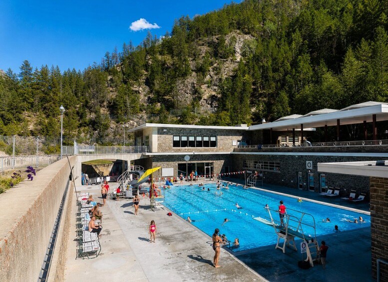 A swimming pool with people in the water, a lifeguard tower, and a building with a clock. 4