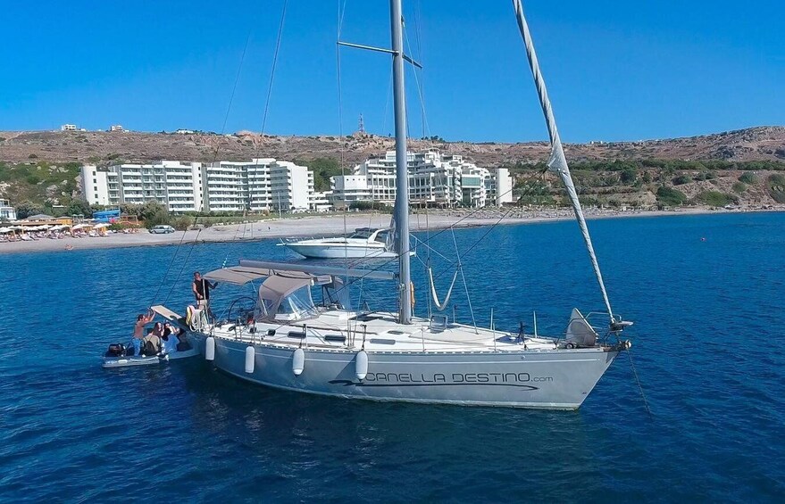 A sailboat named 'Canella Destino' docked near a beach with buildings in the background. 1