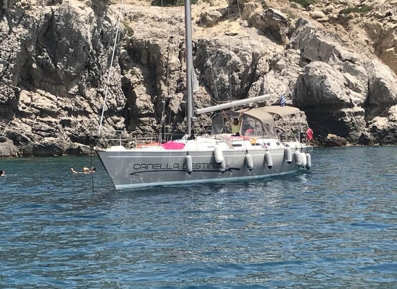 A sailboat named 'CANELLA' anchored near rocky cliffs. 3