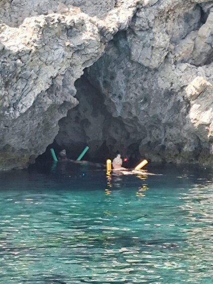A rocky cave entrance with clear water and two people swimming inside. 2