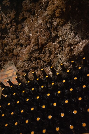 A collection of wine bottles with yellow caps, arranged in rows against a rocky wall. 2