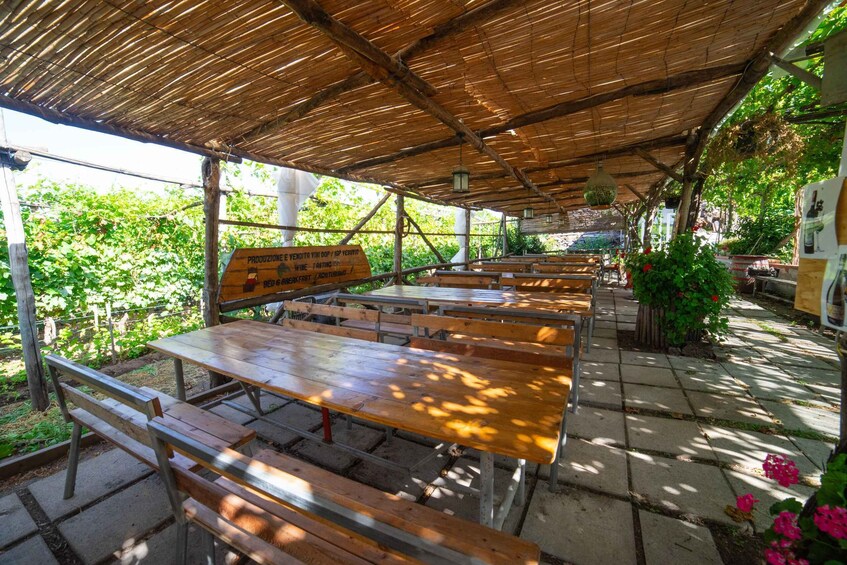 An outdoor seating area with wooden tables and benches under a bamboo roof. 1
