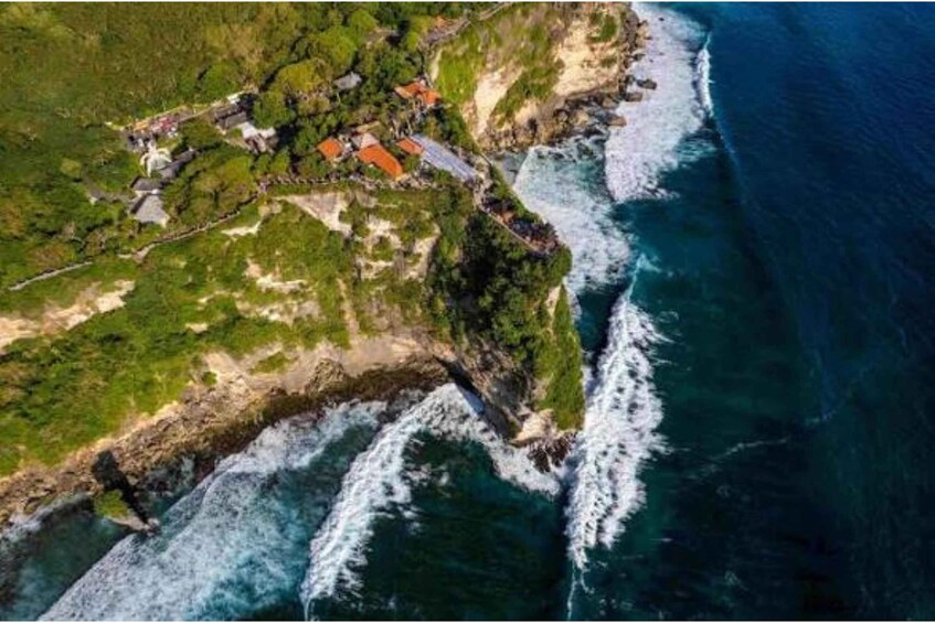 An aerial view of a coastal area with a rocky shoreline, greenery, and a small settlement with red-roofed buildings. 2