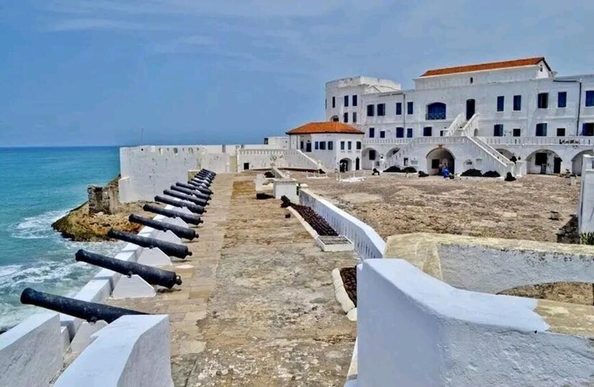 A coastal fort with cannons, a white building with a red roof, and a clear blue sky. 2
