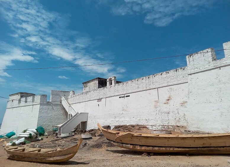 A coastal scene with white walls, a staircase, and two wooden boats on the sand. 4