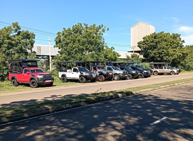 A row of off-road vehicles parked along a roadside with trees and a building in the background. 4