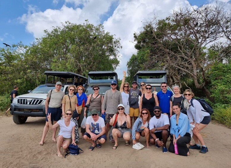 A group of people posing in front of a vehicle with a roof rack, surrounded by trees and a clear sky. 3