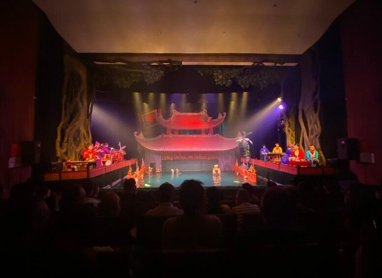 A stage with a traditional Chinese architectural backdrop, performers, and an audience. 4