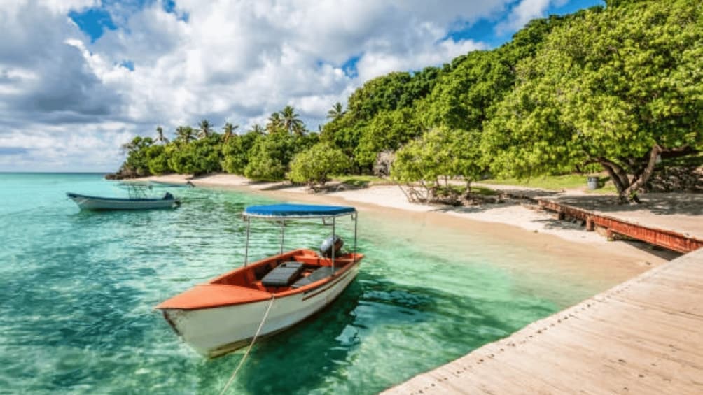 A tropical beach with clear turquoise water, a wooden pier, and boats anchored near the shore. 5