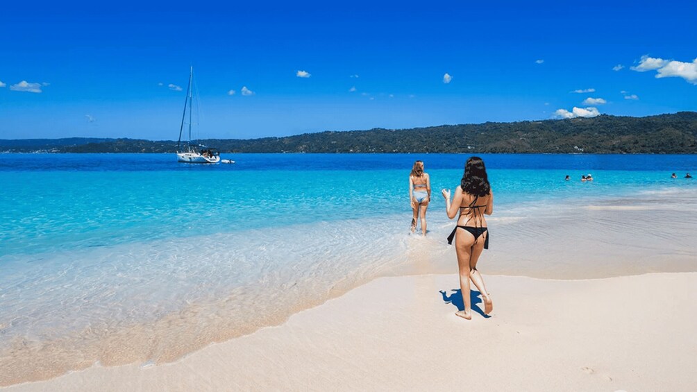 A beach with clear turquoise water, a sailboat, and people in swimwear. 3