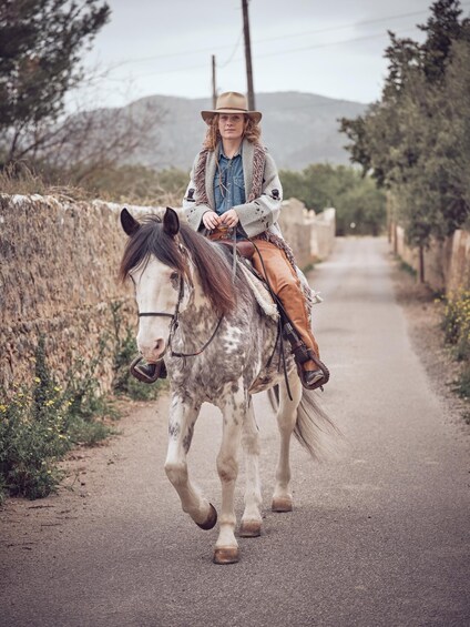 A person riding a horse on a rural road with stone walls and vegetation on either side. 4