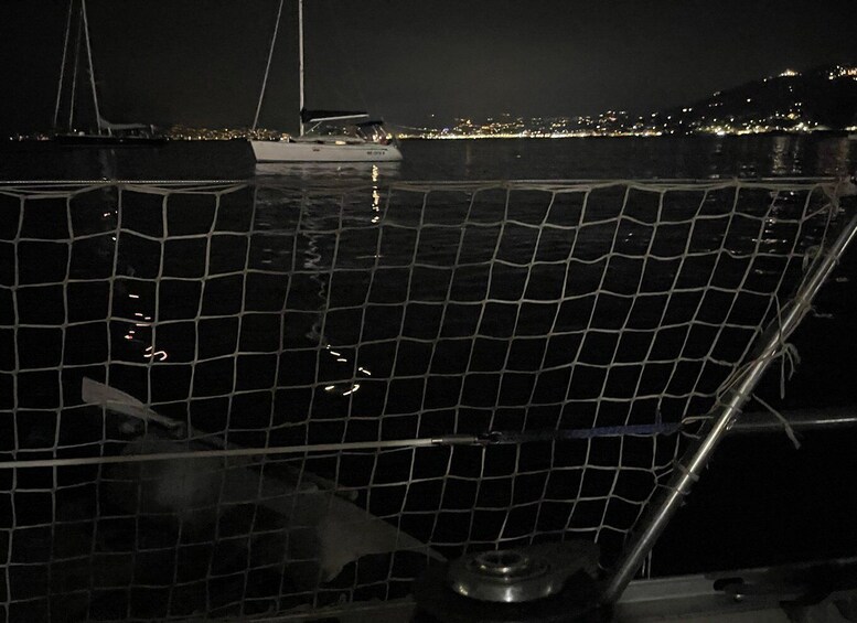A nighttime harbor with a moored sailboat and a cityscape in the background. 3