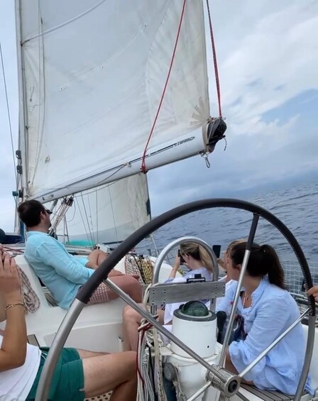 A sailboat with people on deck, a steering wheel, and a clear sky. 2