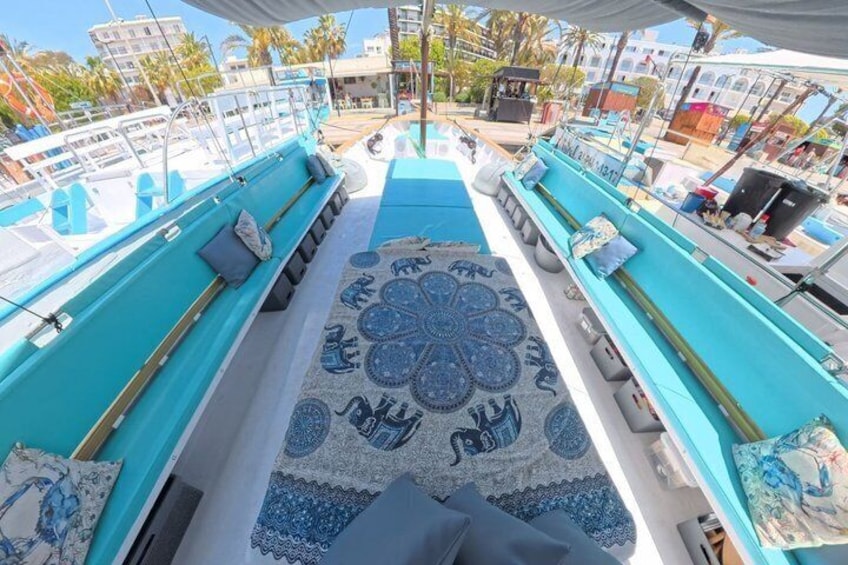 A boat deck with a patterned rug, seating areas, and a view of other boats and buildings. 5