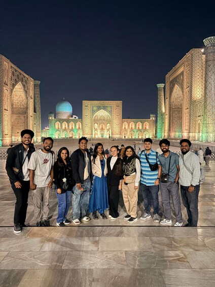 A group of people standing in front of a large, intricately designed building with domes and arches, at night. 3
