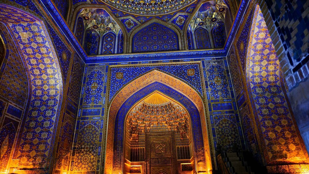 An ornate interior with intricate blue and gold tile work, a large arched doorway, and detailed carvings. 2