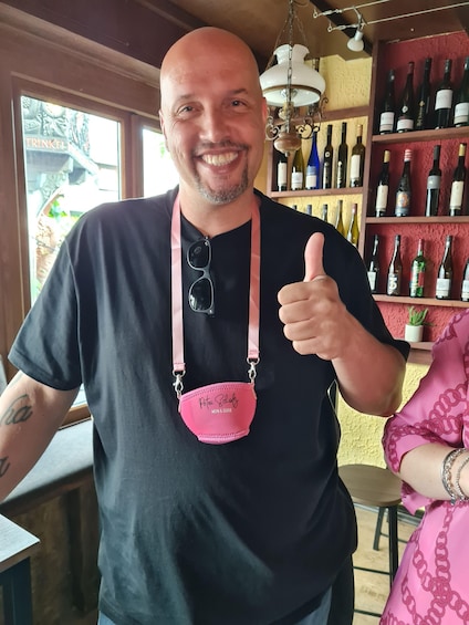A person giving a thumbs-up in a bar with shelves of wine bottles. 3